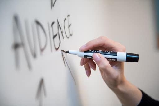 A person writes the word “audience” on a whiteboard with arrows pointing at it.